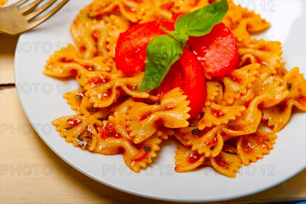 Italian pasta farfalle butterfly bow-tie with tomato basil sauce over white rustic wood table