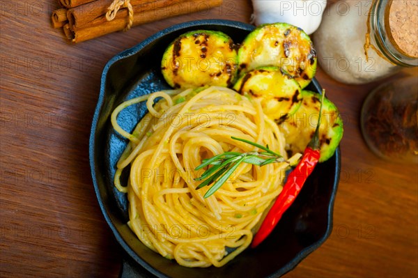 Italian spaghetti pasta with zucchini sauce on iron skillet over wood board