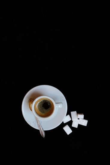 A cup of coffee with sugar cubes on a black background