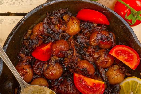 Baby cuttle fish roasted on iron skillet with tomatoes and onions over rustic wood table