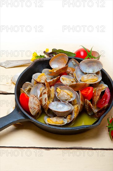 Fresh clams stewed on an iron skillet over wite rustic wood table