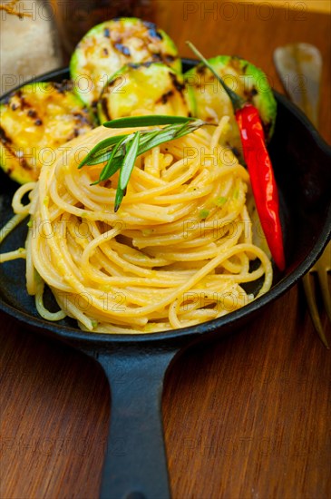 Italian spaghetti pasta with zucchini sauce on iron skillet over wood board