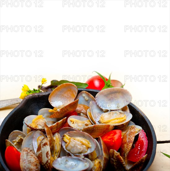 Fresh clams stewed on an iron skillet over wite rustic wood table