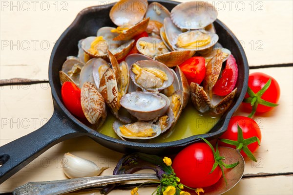 Fresh clams stewed on an iron skillet over wite rustic wood table