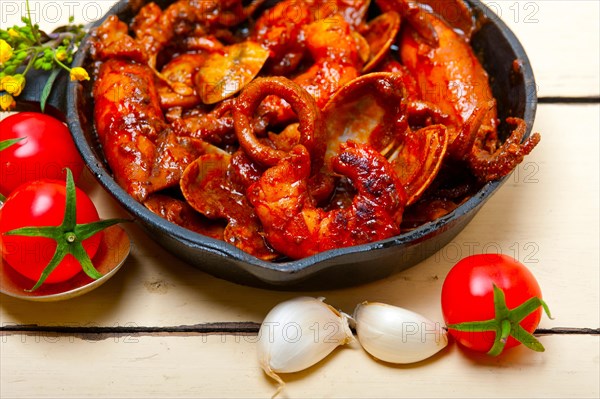 Fresh seafood stew prepared on an iron skillet ove white rustic wood table