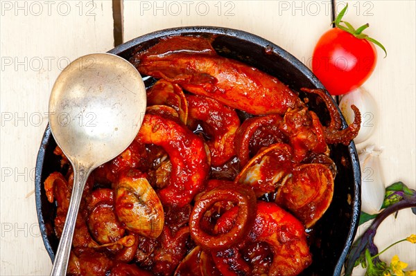 Fresh seafood stew prepared on an iron skillet ove white rustic wood table