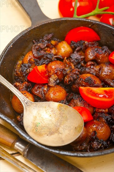 Baby cuttle fish roasted on iron skillet with tomatoes and onions over rustic wood table