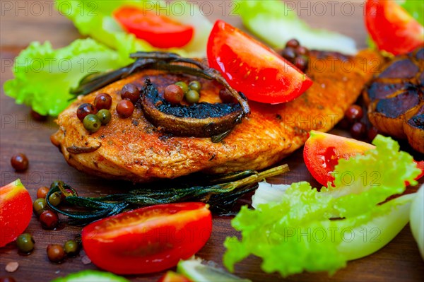 Wood fired hoven cooked chicken breast on wood board with herbs spices and vegetables