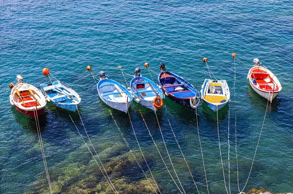 Colourful fishing boats attached to the rock lie in the turquoise water in the harbour of Riomaggiore