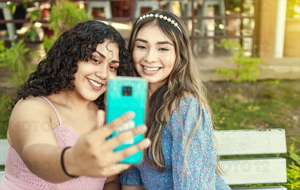 Two pretty girls sitting on a bench taking a selfie