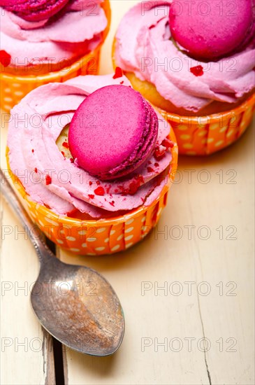 Fresh pink berry cream cupcake with macaroon on top over rustic wood table