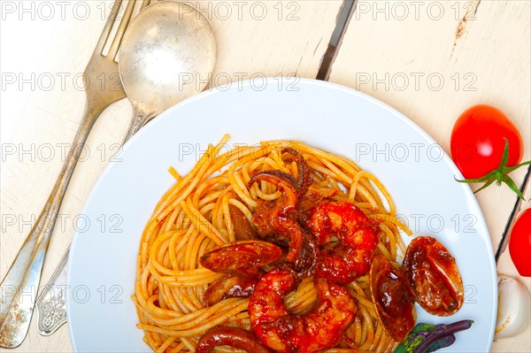 Italian seafood spaghetti pasta on red tomato sauce over white rustic wood table