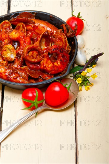 Fresh seafood stew prepared on an iron skillet ove white rustic wood table
