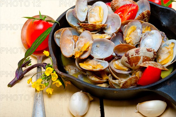 Fresh clams stewed on an iron skillet over wite rustic wood table