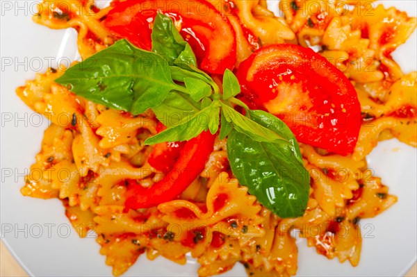 Italian pasta farfalle butterfly bow-tie with tomato basil sauce over white rustic wood table