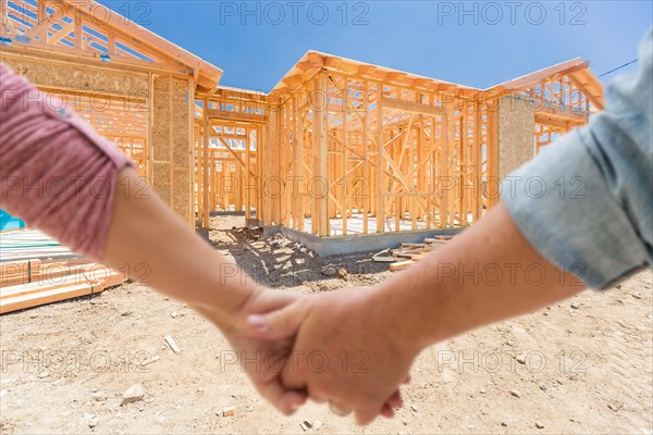 A couple hold his hands and looking at their new house under construction