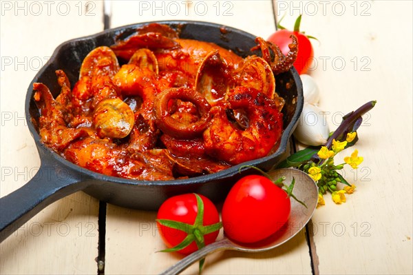 Fresh seafood stew prepared on an iron skillet ove white rustic wood table