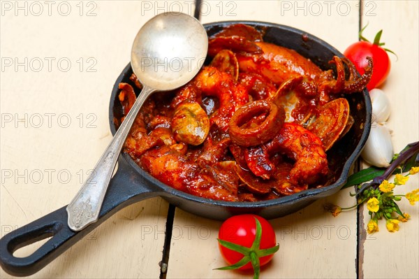 Fresh seafood stew prepared on an iron skillet ove white rustic wood table