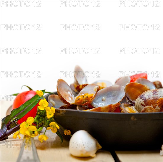 Fresh clams stewed on an iron skillet over wite rustic wood table