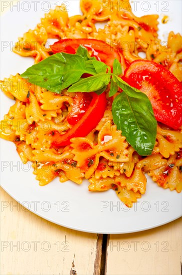 Italian pasta farfalle butterfly bow-tie with tomato basil sauce over white rustic wood table