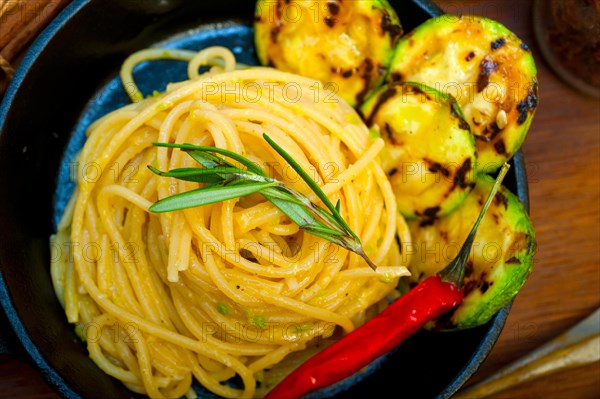 Italian spaghetti pasta with zucchini sauce on iron skillet over wood board