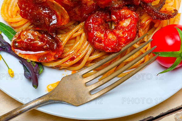 Italian seafood spaghetti pasta on red tomato sauce over white rustic wood table