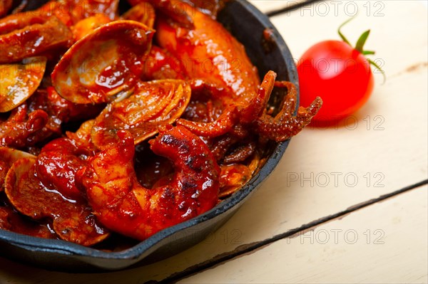 Fresh seafood stew prepared on an iron skillet ove white rustic wood table