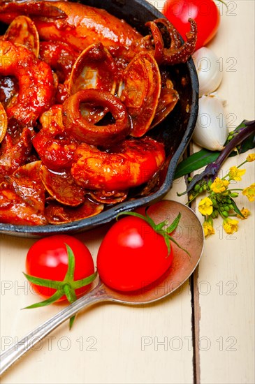 Fresh seafood stew prepared on an iron skillet ove white rustic wood table