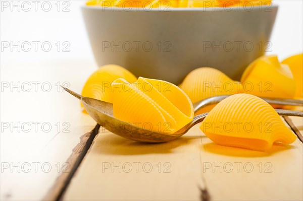 Raw Italian snail lumaconi pasta on a blue bowl over rustic table macro