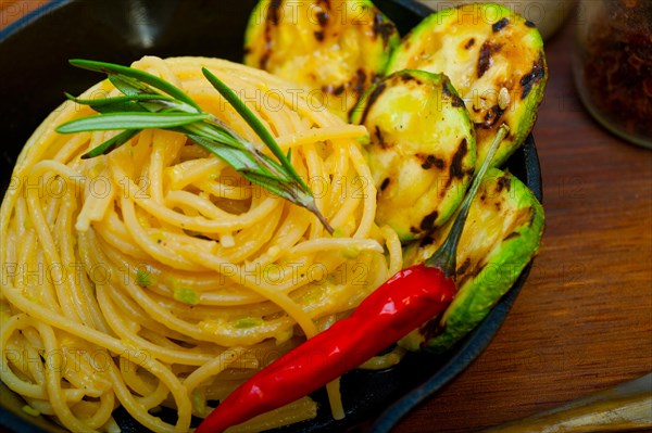 Italian spaghetti pasta with zucchini sauce on iron skillet over wood board