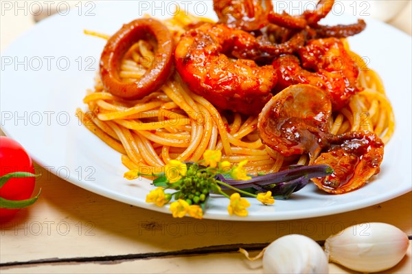 Italian seafood spaghetti pasta on red tomato sauce over white rustic wood table