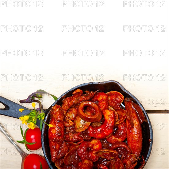 Fresh seafood stew prepared on an iron skillet ove white rustic wood table