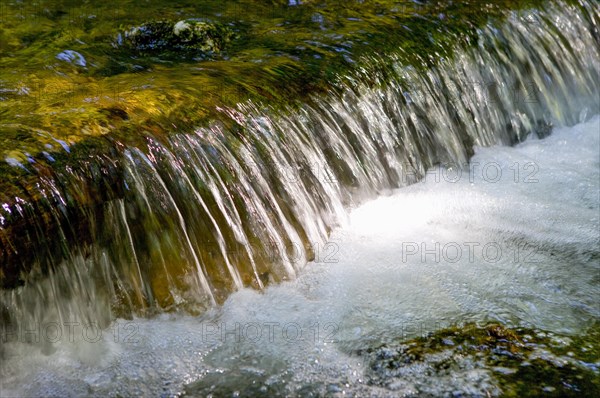 Flowing water with small waterfall and light reflections