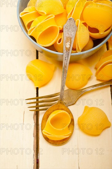 Raw Italian snail lumaconi pasta on a blue bowl over rustic table macro