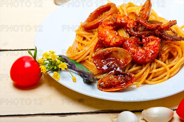 Italian seafood spaghetti pasta on red tomato sauce over white rustic wood table