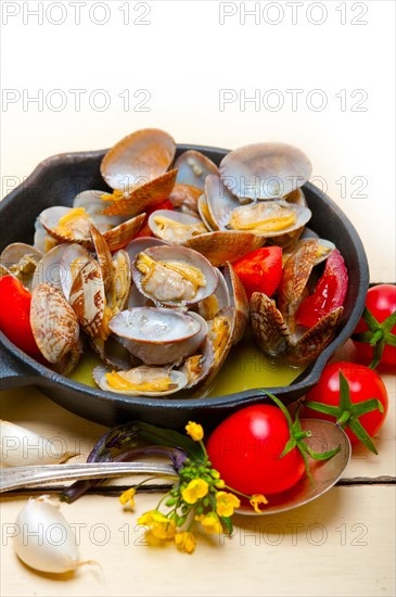 Fresh clams stewed on an iron skillet over wite rustic wood table