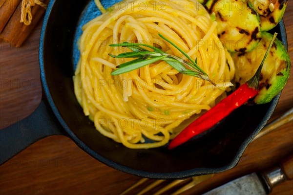 Italian spaghetti pasta with zucchini sauce on iron skillet over wood board