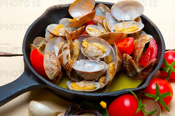 Fresh clams stewed on an iron skillet over wite rustic wood table