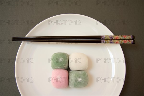 Four Japanese mochi sweets with chopsticks on a porcelain plate