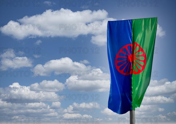 Eine Roma und Sintiflagge weht im Wind mit Wolken als Hintergrund