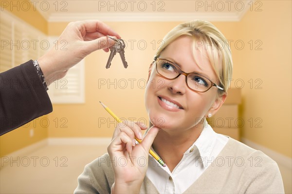 Woman holding pencil being handed keys in empty room with boxes