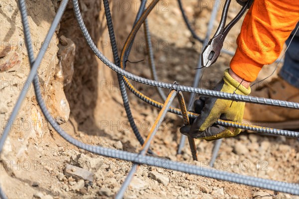 Worker securing steel rebar framing with wire plier cutter tool at construction site