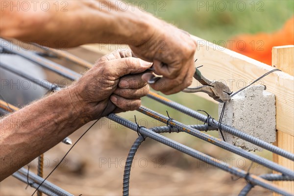 Worker securing steel rebar framing with wire plier cutter tool at construction site