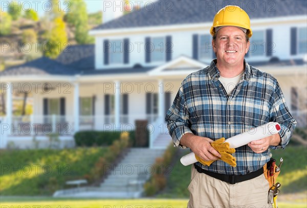 Contractor with plans and hard hat in front of beautiful custom house