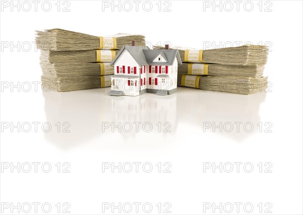 Stacks of one hundred dollar bills with small house on slight reflective surface