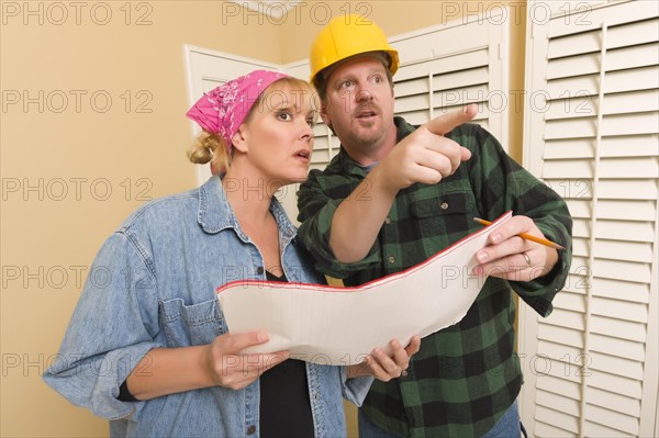 Male contractor in hard hat discussing plans with woman in room