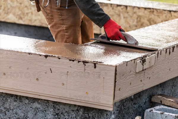 Construction worker using wood trowel on wet cement forming coping around new pool