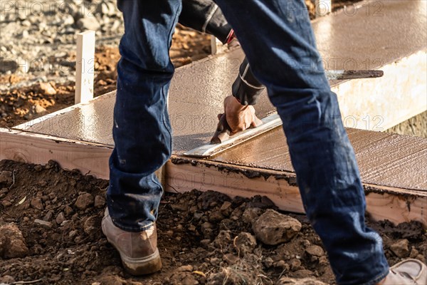 Construction worker using wood trowel on wet cement forming coping around new pool