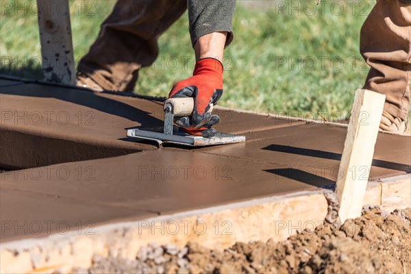 Construction worker using hand groover on wet cement forming coping around new pool