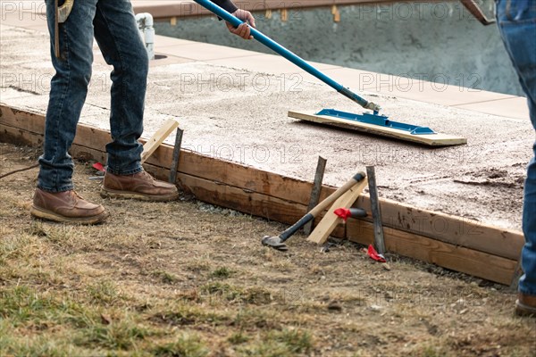 Construction worker smoothing wet cement with trowel tool